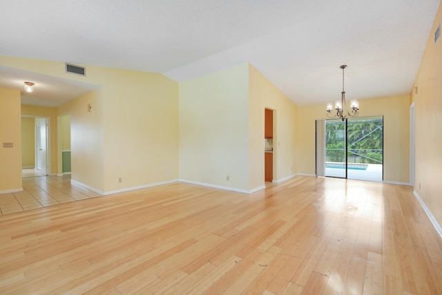 unfurnished room featuring lofted ceiling, light wood-type flooring, visible vents, and a notable chandelier