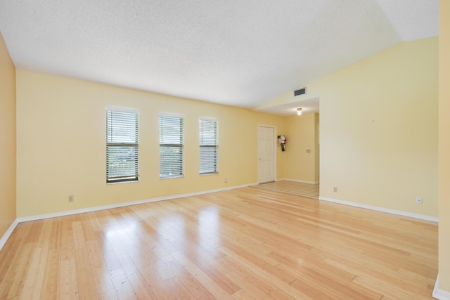 spare room featuring baseboards, visible vents, vaulted ceiling, a textured ceiling, and light wood-style floors