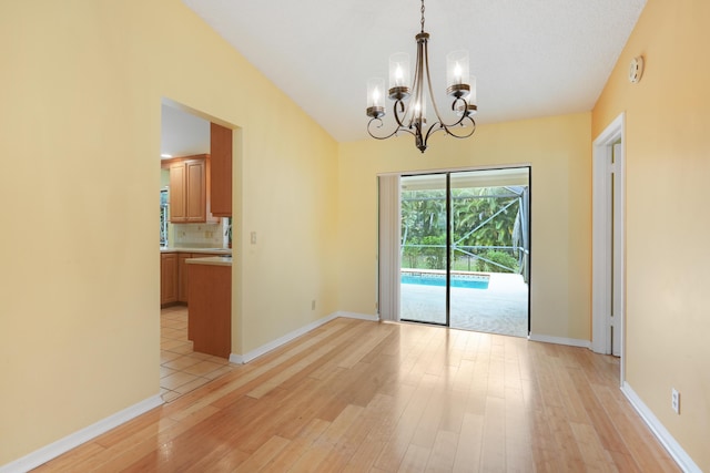 unfurnished dining area with light wood-style floors, a chandelier, vaulted ceiling, and baseboards