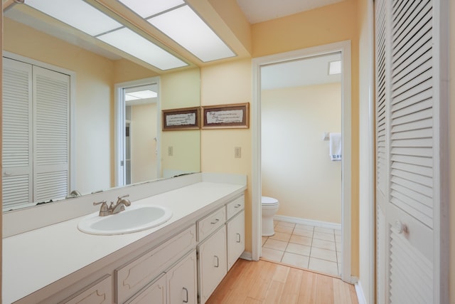 bathroom featuring toilet, a closet, wood finished floors, and vanity