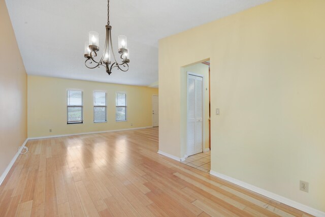 spare room featuring light wood-type flooring, baseboards, and an inviting chandelier