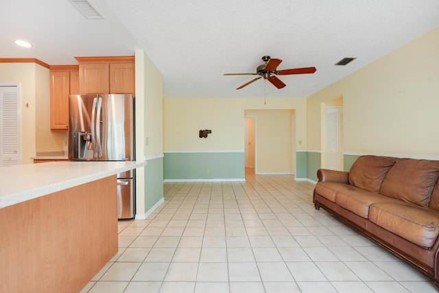 living room featuring light tile patterned floors, a textured ceiling, visible vents, and a ceiling fan