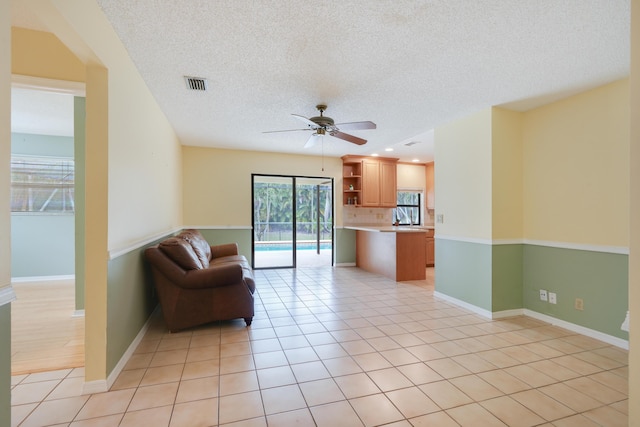 unfurnished living room featuring ceiling fan, a textured ceiling, light tile patterned flooring, visible vents, and baseboards