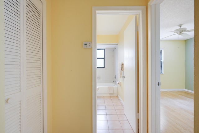 hallway with a textured ceiling, baseboards, and light tile patterned floors