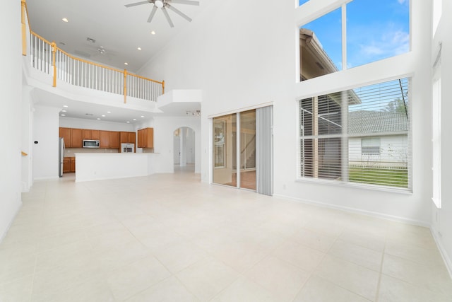 unfurnished living room featuring arched walkways, recessed lighting, a towering ceiling, a ceiling fan, and baseboards