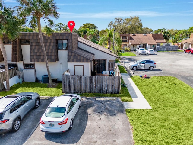 view of front of home with mansard roof, a residential view, stucco siding, uncovered parking, and a front yard