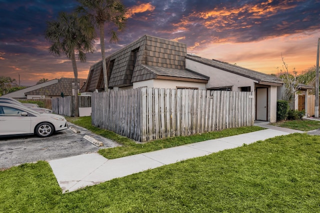 view of property exterior featuring mansard roof, a lawn, fence, uncovered parking, and stucco siding