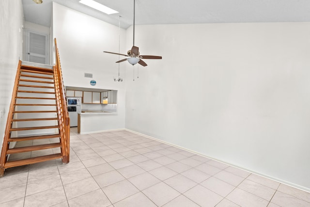 unfurnished living room featuring visible vents, ceiling fan, stairway, a skylight, and high vaulted ceiling