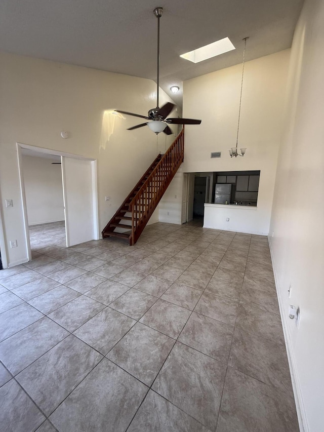 unfurnished living room with tile patterned floors, stairway, a high ceiling, a skylight, and ceiling fan