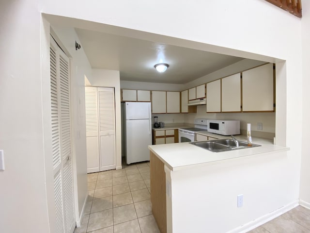 kitchen with light countertops, cream cabinets, a sink, white appliances, and a peninsula