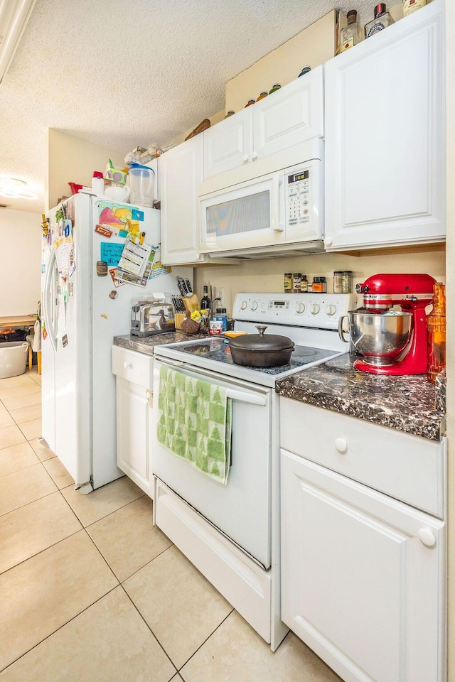 kitchen with dark countertops, light tile patterned flooring, white cabinets, a textured ceiling, and white appliances