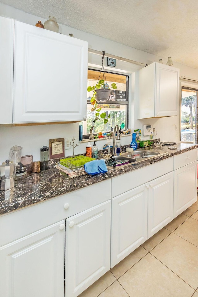 kitchen featuring plenty of natural light, dark stone countertops, white cabinetry, and a sink