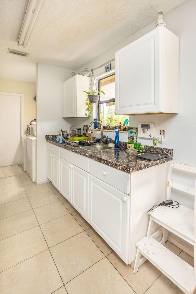 kitchen with visible vents, white cabinetry, a sink, light tile patterned flooring, and independent washer and dryer