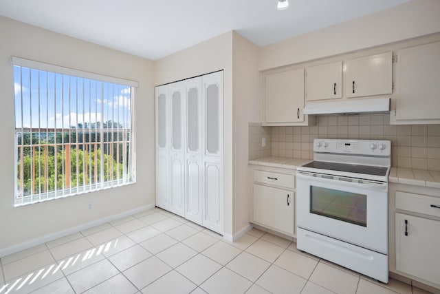 kitchen featuring light tile patterned floors, tasteful backsplash, white range with electric cooktop, white cabinets, and under cabinet range hood