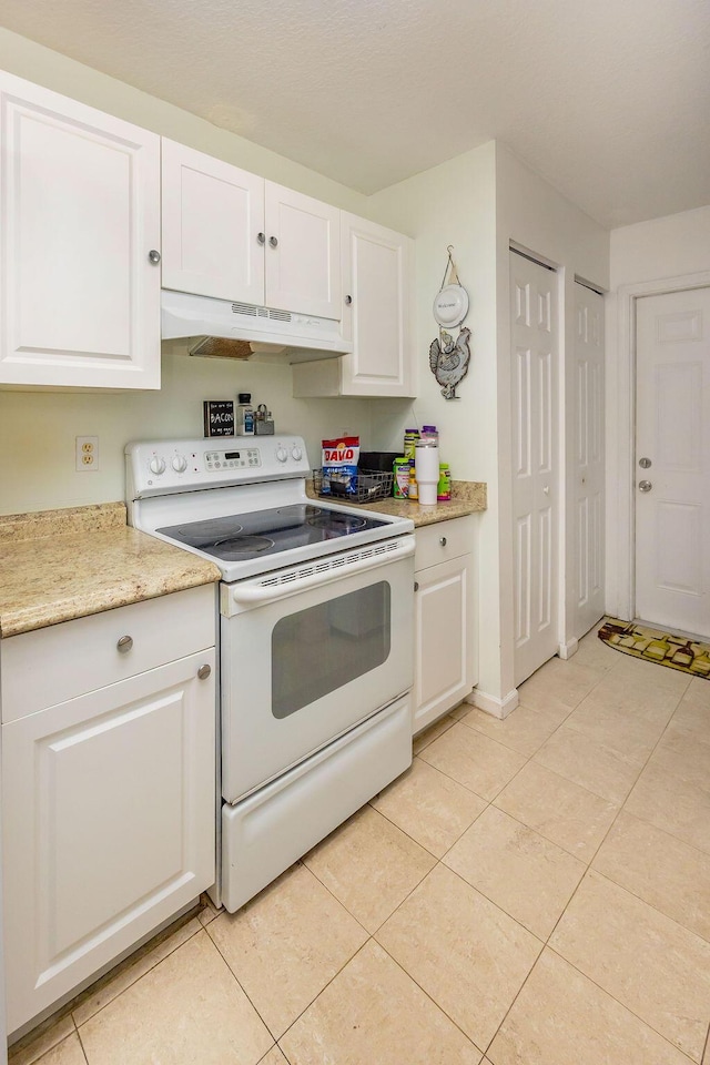 kitchen with light tile patterned floors, electric stove, white cabinetry, and under cabinet range hood