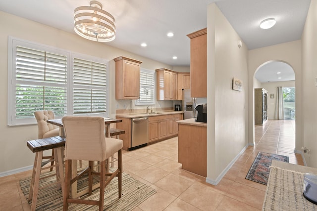 kitchen with arched walkways, light tile patterned floors, light countertops, appliances with stainless steel finishes, and light brown cabinetry