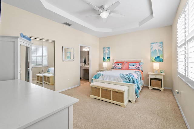 bedroom featuring light carpet, baseboards, multiple windows, and a tray ceiling