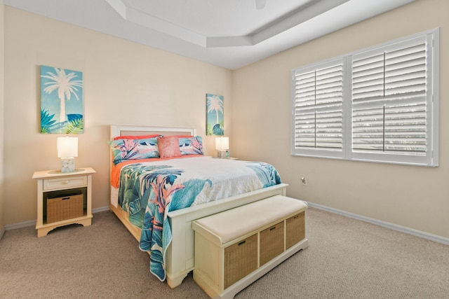 bedroom featuring a tray ceiling, light carpet, and baseboards