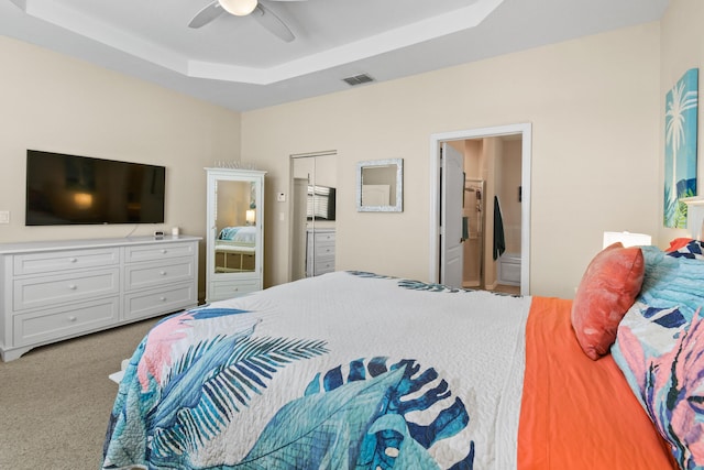 bedroom with carpet, visible vents, a tray ceiling, and a ceiling fan