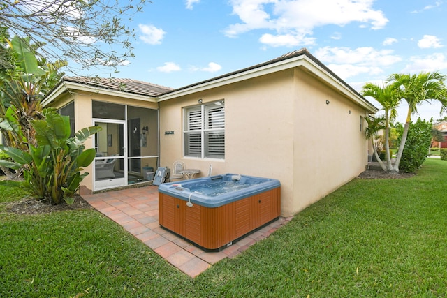 rear view of property with a patio, stucco siding, a lawn, a hot tub, and a sunroom