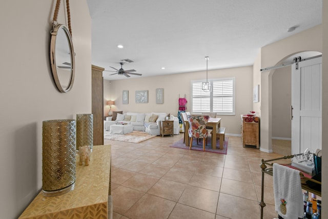 living room featuring ceiling fan, a barn door, light tile patterned flooring, visible vents, and baseboards