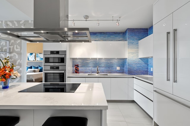 kitchen with built in refrigerator, island exhaust hood, white cabinetry, and a sink