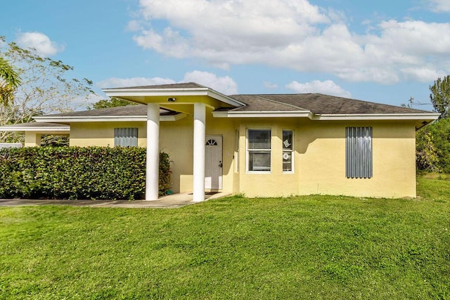 rear view of house featuring a lawn and stucco siding