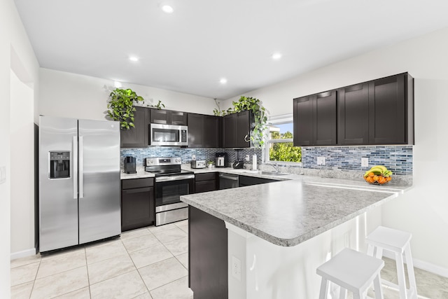 kitchen featuring a breakfast bar area, stainless steel appliances, tasteful backsplash, a sink, and a peninsula