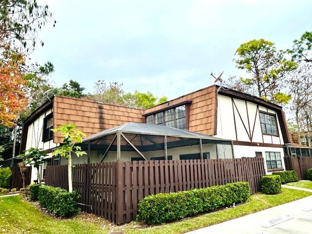 view of property exterior featuring a lanai, fence, and a gambrel roof