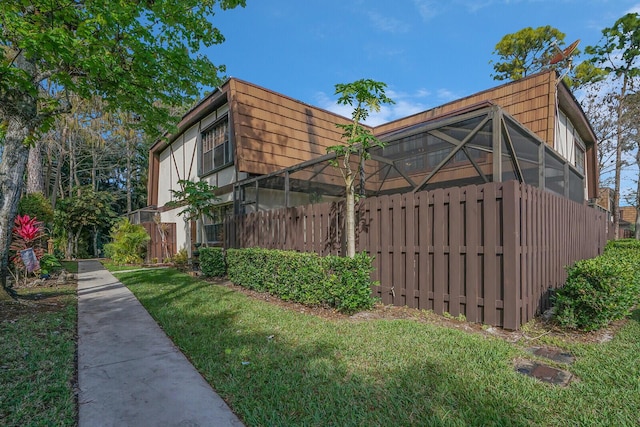 view of side of property with glass enclosure, fence, mansard roof, and a yard