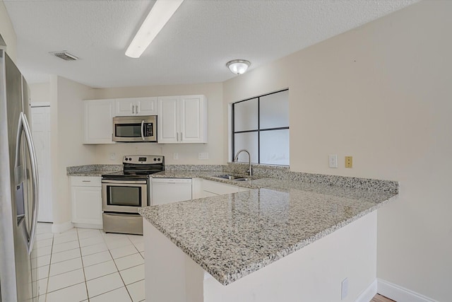 kitchen with white cabinets, appliances with stainless steel finishes, a peninsula, light stone countertops, and a sink