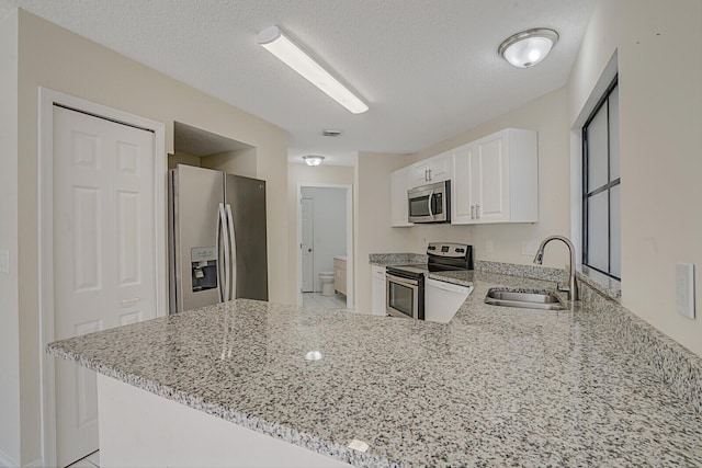 kitchen with a peninsula, appliances with stainless steel finishes, a sink, and white cabinets