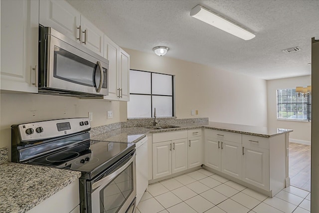 kitchen with visible vents, appliances with stainless steel finishes, a peninsula, white cabinetry, and a sink