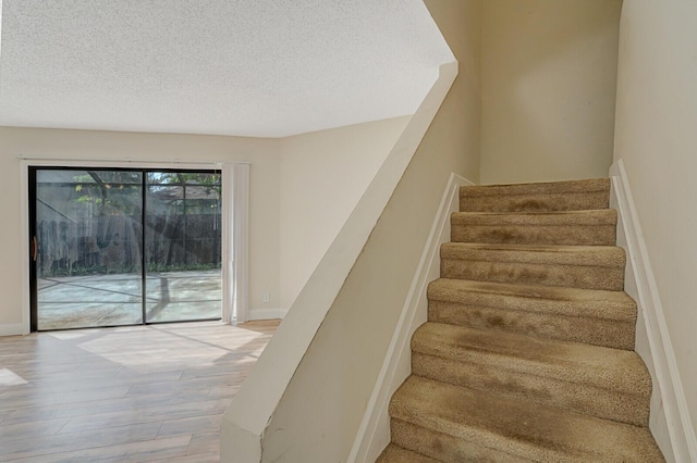 staircase featuring a textured ceiling, baseboards, and wood finished floors