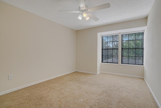 spare room with ceiling fan, baseboards, a textured ceiling, and light colored carpet