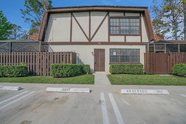 view of front of property featuring a front yard, glass enclosure, uncovered parking, and stucco siding