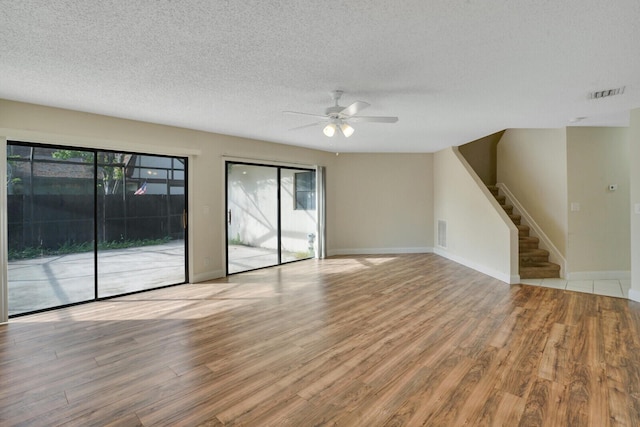 unfurnished living room featuring stairs, light wood finished floors, a textured ceiling, and plenty of natural light