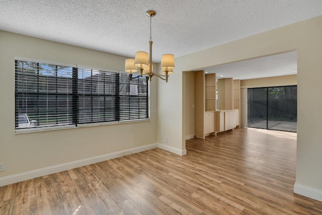 empty room with a textured ceiling, wood finished floors, a healthy amount of sunlight, baseboards, and an inviting chandelier