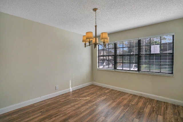 empty room featuring a textured ceiling, baseboards, a chandelier, and dark wood-type flooring