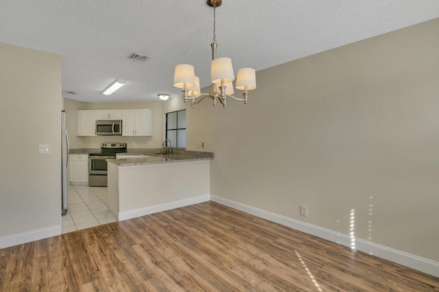 kitchen with decorative light fixtures, a peninsula, stainless steel appliances, light wood-type flooring, and white cabinetry