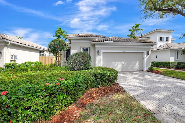 mediterranean / spanish-style home featuring decorative driveway, a tile roof, an attached garage, and stucco siding