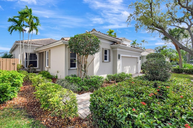 view of home's exterior with a garage, a tile roof, fence, and stucco siding