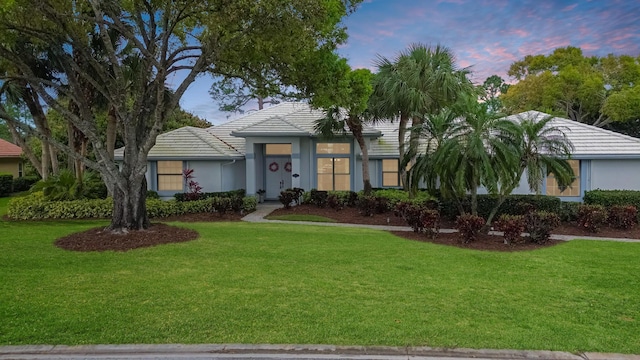 ranch-style home with stucco siding, a tiled roof, and a yard