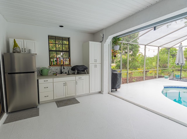 kitchen with light floors, white cabinets, a sink, and freestanding refrigerator