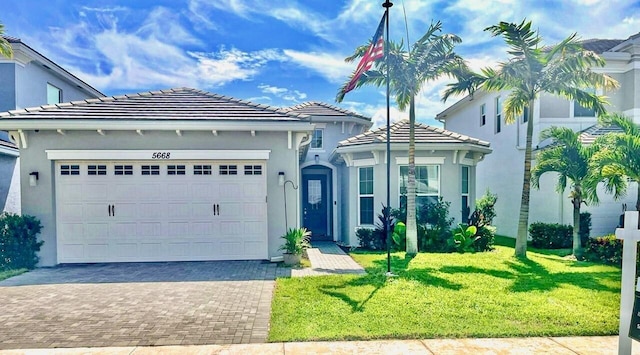 view of front of home featuring decorative driveway, stucco siding, a front yard, a garage, and a tiled roof