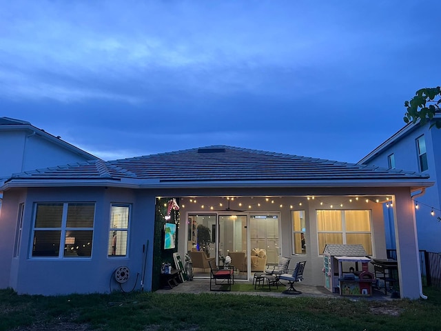 back of house featuring a patio, a lawn, a tiled roof, and stucco siding