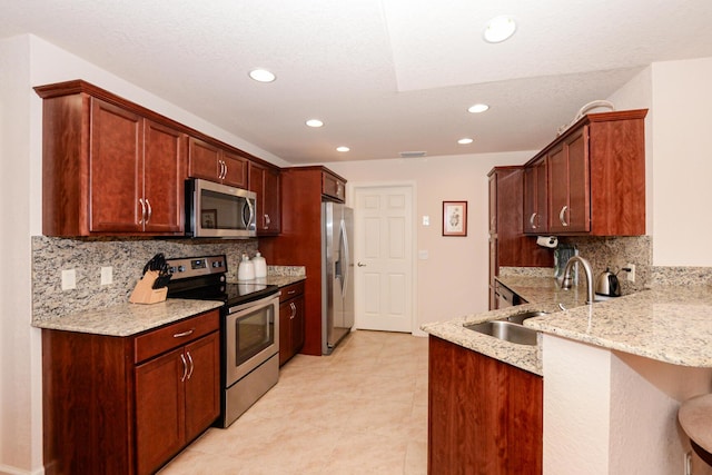 kitchen featuring a breakfast bar area, stainless steel appliances, a sink, light stone countertops, and a peninsula