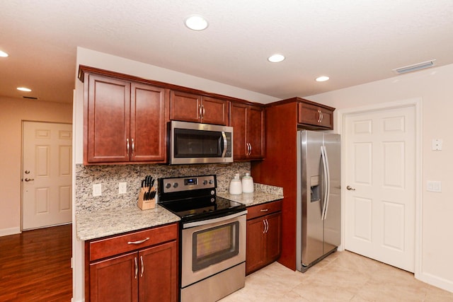 kitchen featuring light stone counters, visible vents, stainless steel appliances, and backsplash