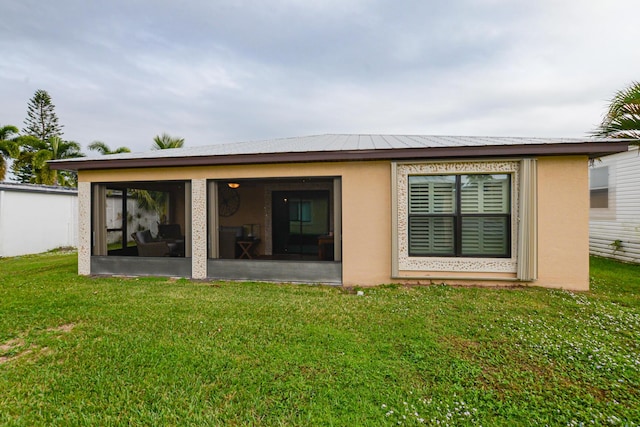 rear view of house featuring a sunroom, a yard, metal roof, and stucco siding