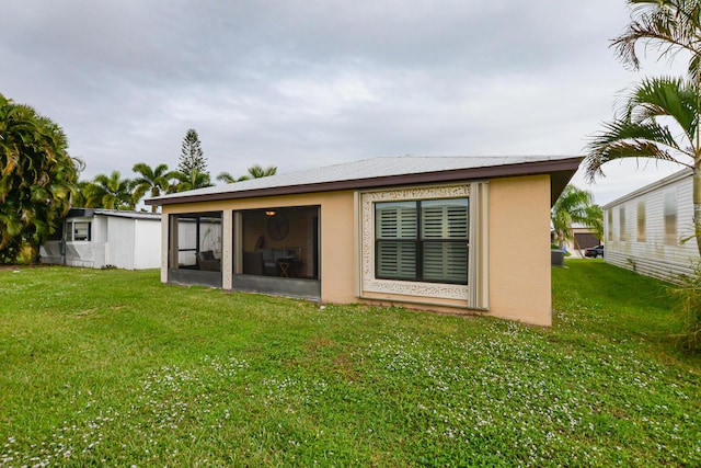 back of property featuring a sunroom, a lawn, and stucco siding